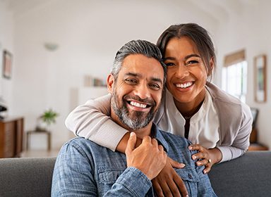Portrait of multiethnic couple embracing and looking at camera sitting on sofa.
